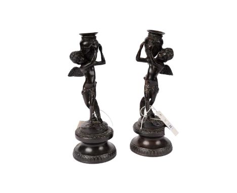 A pair of bronze candlesticks, in the form of putti carrying urns, raised on tapered circular bases, 27.5cms high.