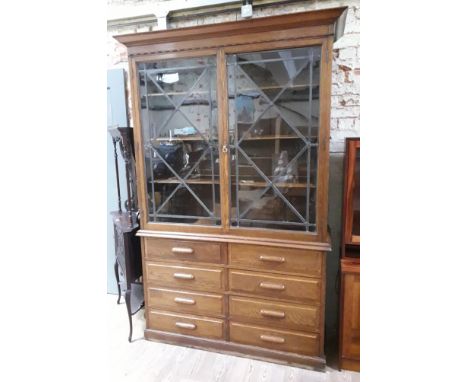 A large oak cabinet bookcase circa 1920 with leaded glass panel doors above eight lower drawers with cup handles, width 154cm