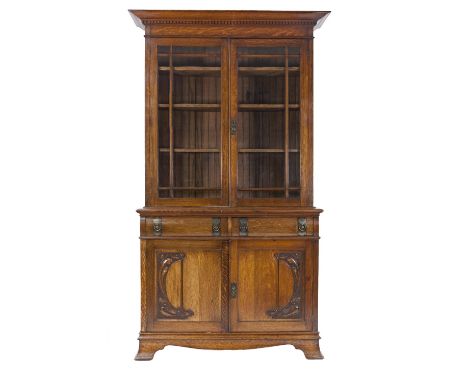 EARLY TWENTIETH CENTURY ARTS AND CRAFTS CARVED OAK LIBRARY BOOKCASE, the dentil moulded cornice above a pair of glazed cupboa