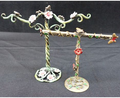 TWO ENAMELLED METAL RING STANDS cast with flowers and butterflies, each set with paste stones, the largest 11cm high 