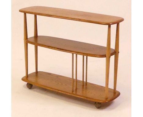 A 1960s Ercol blond elm Windsor 361 'Baby Giraffe' three-tier bookcase trolley, with divisional lower section, raised on roll