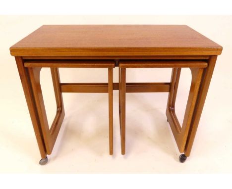 A 1970s teak nest of three occasional tables, by A.H. McIntosh, the largest with swivel fold-over top, raised on roller casto