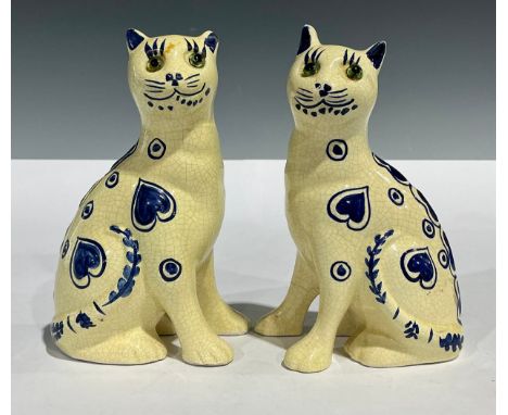 A pair of Emile Galle style pottery cats, tin glazed and decorated with blue hearts and dots, glass eyes, unmarked, 15cm high