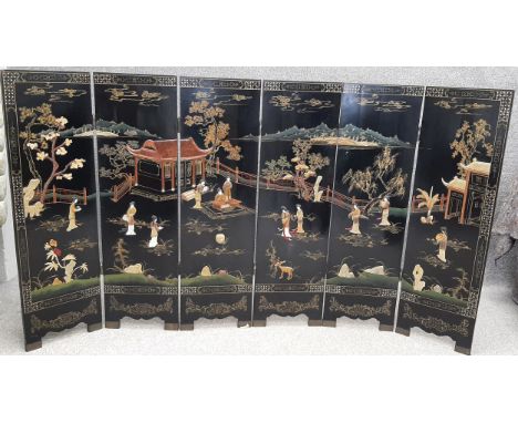 A mid 20th century Chinese lacquer and carved soapstone six panel folding screen depicting a seated emperor in front of a pag