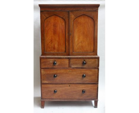 An early 19th century small mahogany linen press, carved overhanging cornice over two doors, above two small drawers over two