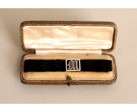 A 20th century gold and gem chipping ribbon bracelet with centred M surrounded by enamel border and adjustable strap, in box