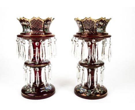 A pair of Edwardian cranberry glass table lustres, having gilt and enamel floral decoration and cut crystal drops, with two c