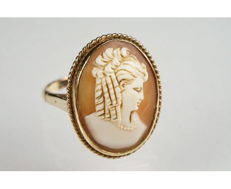 Shell cameo yellow gold ring, the oval cameo depicting female profile with ringlet hair facing right, rubover set, rope twist