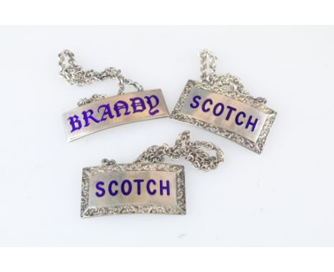 Pair of silver rectangular Scotch decanter labels, blue enamelled "Scotch" to both, cast foliate scroll border in relief, mak