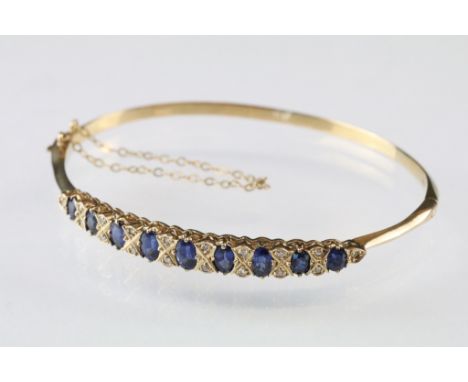 Sapphire and diamond 9ct yellow gold hinged bangle, nine graduated oval mixed cut sapphires, the principal sapphire measuring