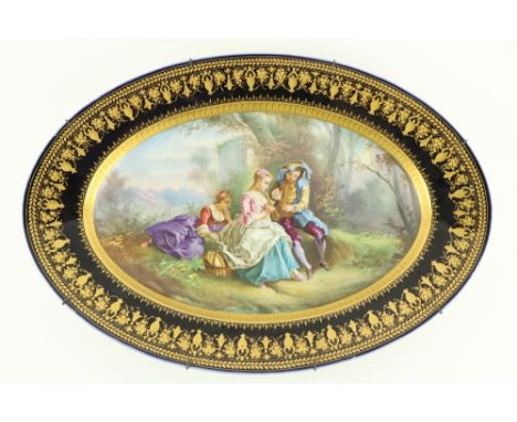 A large oval Serves style porcelain Platter, depicting three figures in a garden landscape, inside a dark blue and gilt decor