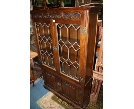 A reproduction Oak ''Old Charm'' style glazed Bookcase on Cupboard, having plain top over carved frieze, over pair of opposin