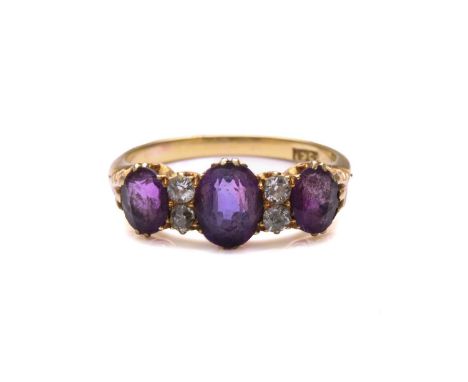 An amethyst and diamond half hoop ring, comprising three graduated oval-shaped amethysts, claw set in scrolled mounts with ol