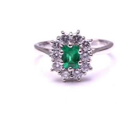 An emerald and diamond entourage ring in 18ct white gold, featuring an emerald-cut emerald of 4.9 x 3.8 mm in bright green co