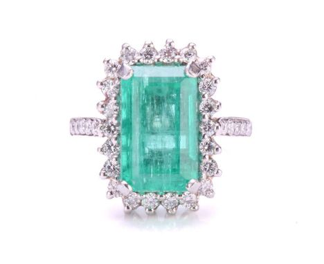 An emerald and diamond halo ring in platinum, featuring a rectangular emerald-cut emerald with bright green colour, approxima