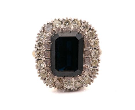 A sapphire and diamond cluster ring in 18ct gold, featuring an emerald-cut sapphire with a dark blue body colour that display