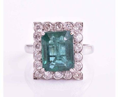 An emerald and diamond halo ring, consisting of a central emerald approximately measuring 10.9 x 8.7 mm, claw set on a white 