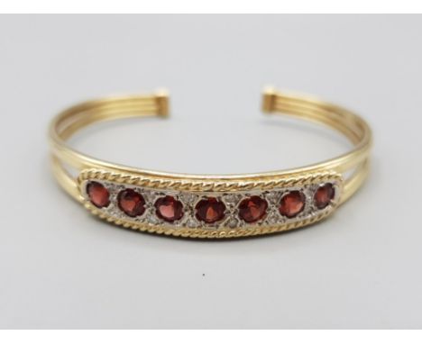 Ladies 9ct yellow gold stone set torque bangle, featuring 7 round red stones set with 2 white stones in between ( 12 intotal 