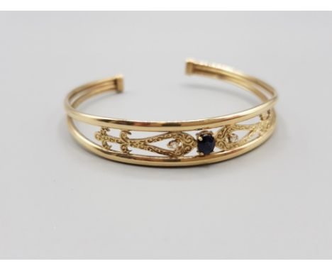 Ladies 9ct yellow gold ornate stone set bangle, featuring a oval shaped sapphire set in the centre with a single white stone 