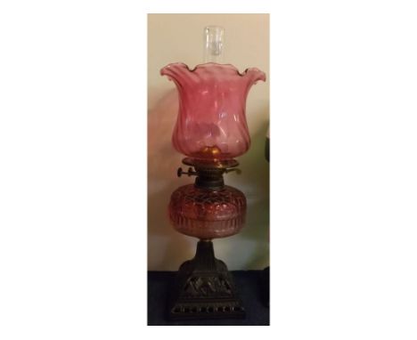 Victorian black cast iron based oil lamp with cranberry font and crimped edge shade, 22ins tall  