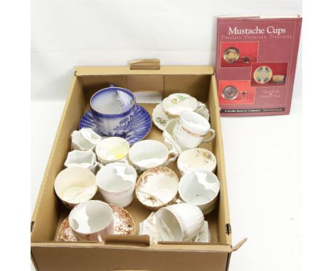 Victorian and later porcelain moustache cups, some with saucers, and related book, in one box