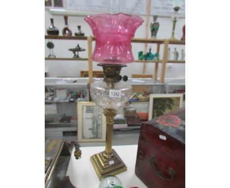 A brass Corinthian column oil lamp with cut glass font and acid etched cranberry glass shade