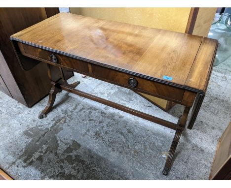 A reproduction mahogany sofa table with drop side flaps, two frieze drawers on trestle ends and fluted splayed legs with lion