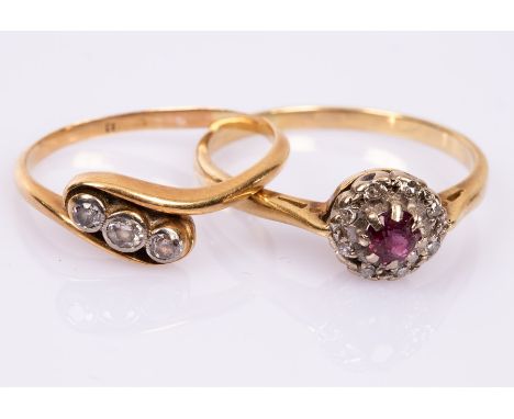 A ruby and diamond cluster ring, set in 18ct yellow gold, size U and a diamond three-stone ring in 18ct yellow gold crossover