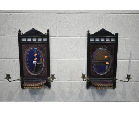 A PAIR OF EARLY 20TH CENTURY EBONISED GIRANDOLES, with an oval mirror, two brass candle holders flanking a shelf, width 30cm 