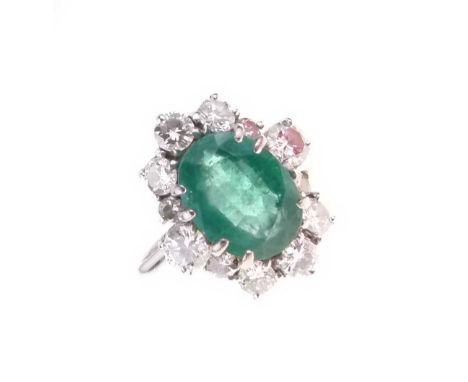 Emerald and diamond cluster ring, in 18ct white gold, 1975, the oval cut enclosed by twelve brilliant cuts estimated as total