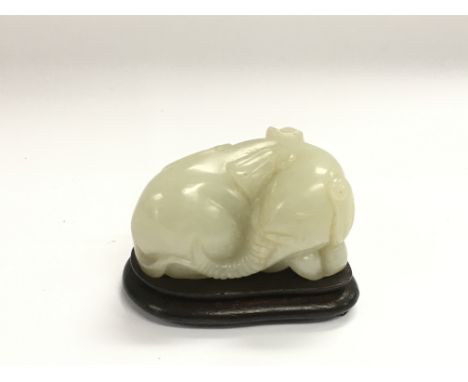 A jade figure of a recumbent elephant raised on a hardwood stand, approx length 6cm.