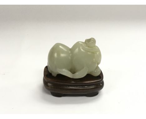 A jade figure of two peaches and a monkey raised on a hardwood stand, approx length 5cm.
