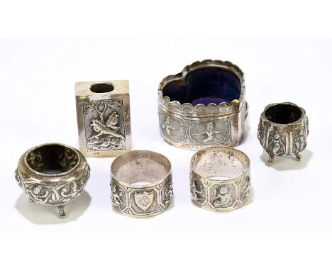 A small group of Indian white metal to include a matchbox case, embossed decorated with a lion in landscape, a pair of napkin