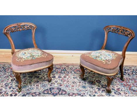 A pair of Victorian carved walnut framed nursing chairs with tapestry seats terminating on brass castors.