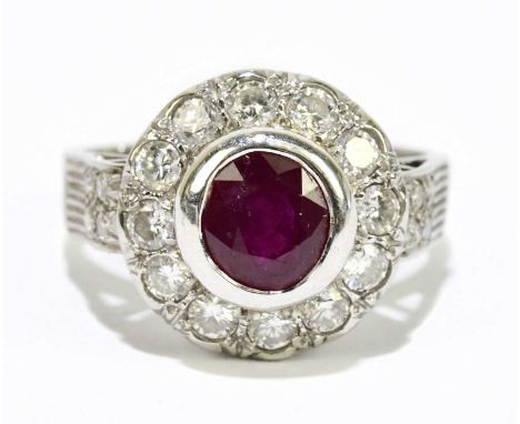 A white metal diamond and ruby ring, stamped '750', with central collet set ruby within a border of round brilliant cut diamo