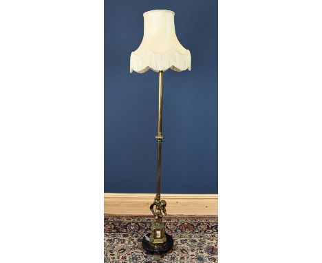 A gilt brass standard lamp, with cherub base supported on a canted square section with printed ceramic mounts, on paw shaped 
