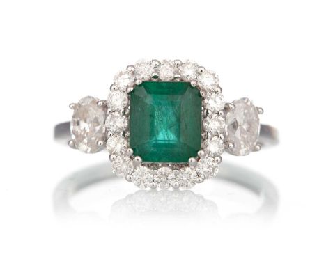 EMERALD AND DIAMOND RING, set with an octagonal step cut emerald within a halo of diamonds and flanked by two oval diamonds o