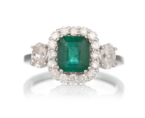 EMERALD AND DIAMOND RING, set with an octagonal step cut emerald within a halo of diamonds and flanked by two oval diamonds o