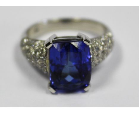  A Tanzanite And Diamond Ring centred with a cushion-cut tanzanite weighing 5.147ct, the band pave-set with round brilliant-c