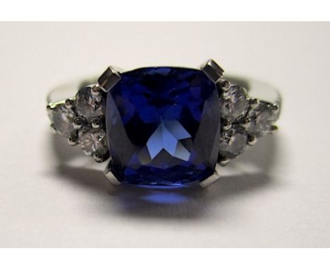 A Tanzanite And Diamond Ring centred with a cushion-cut tanzanite weighing approximately 3.30ct, flanked by tri-set round bri