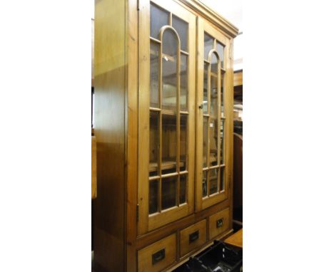A pine bookcase with glazed doors, fitted shelves, drawers under, on bracket feet
