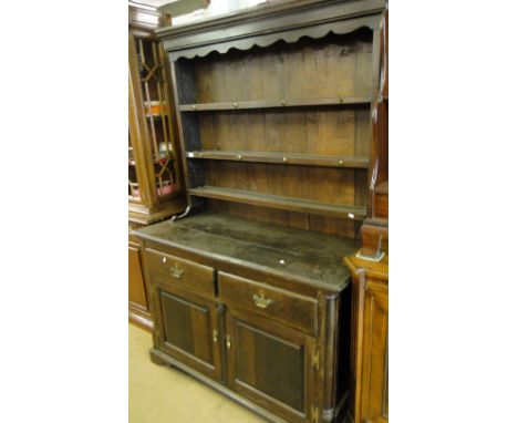 An 18th century oak dresser, with open plate rack, the base fitted with 2 drawers and fielded panelled cupboards, bracket fee