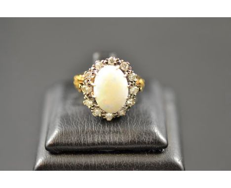 An 18ct gold ring with scroll detail to shoulders, set with central opal surrounded by twelve diamonds - size N.  CONDITION R