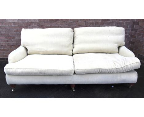 A LARGE SOFA  by 'The Sofa Works', upholstered in pale yellow with loose cushions, the three frontal supports raised on brass