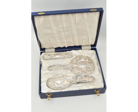 A CASED SILVER MOUNTED DRESSING TABLE SET, to include two brushes, a mirror and comb, with embossed scrolling floral and foli