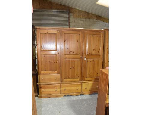 A modern pine triple wardrobe Having a moulded cornice above an arrangement of two long panelled doors, a short door and four