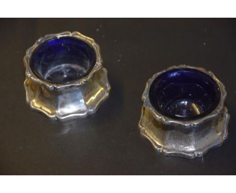 A pair of silver saltsEach with an octagonal base and grooved body to the scrolling rim, containing blue glass liners, James 