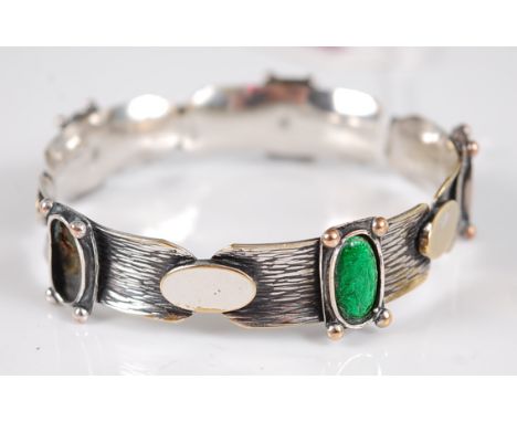 An Arts &amp; Crafts bangle, the 12mm wide textured bangle set with oval collet mounted green enamel discs with beaded corner