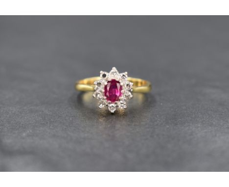 An 18ct gold ruby and diamond cluster ring having a central diamond within a surround of ten small diamonds in a claw set bas