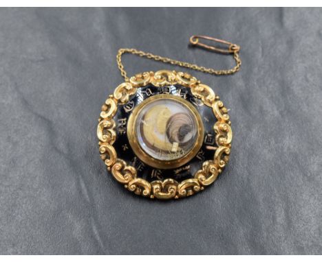 A Victorian yellow metal hair mourning brooch, of circular form having scroll decoration with black enamel inscribed 'In Memo